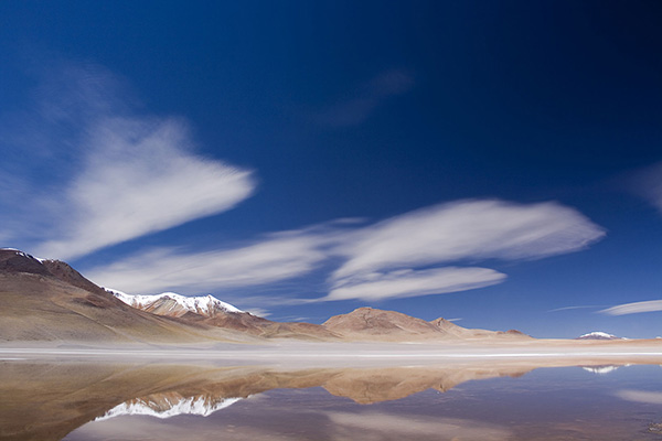 montanhas no horizonte, refletidas no lago à frente, sob um céu azul, no planalto boliviano.